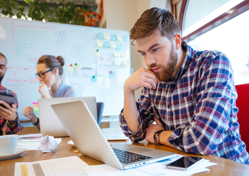 a concentrated bearded young man using laptop 